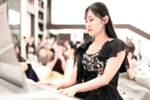 披露宴会場で黒いドレスを着てピアノを演奏する女性。結婚式の余興や音楽演出でゲストへ感動を届ける、真剣な表情が印象的なウェディングスナップ。